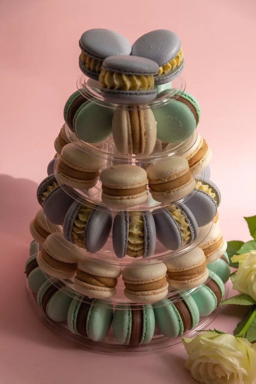 A tiered macaron tower in lavender, mint and cream, with white roses beside it.